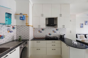 A compact kitchen with white cabinets, a black stove, and a water dispenser. - Céleste Skies by Redolive Nr Manipal Whitefield (Bengaluru)