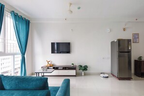 A modern living room with a sofa, a TV mounted on the wall, a small table with a decorative item, and a refrigerator. - Céleste Skies by Redolive Nr Manipal Whitefield (Bengaluru)