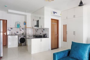 A modern kitchen with a washing machine, a coffee maker, and a stove. There is a blue sofa in the living area. - Céleste Skies by Redolive Nr Manipal Whitefield (Bengaluru)