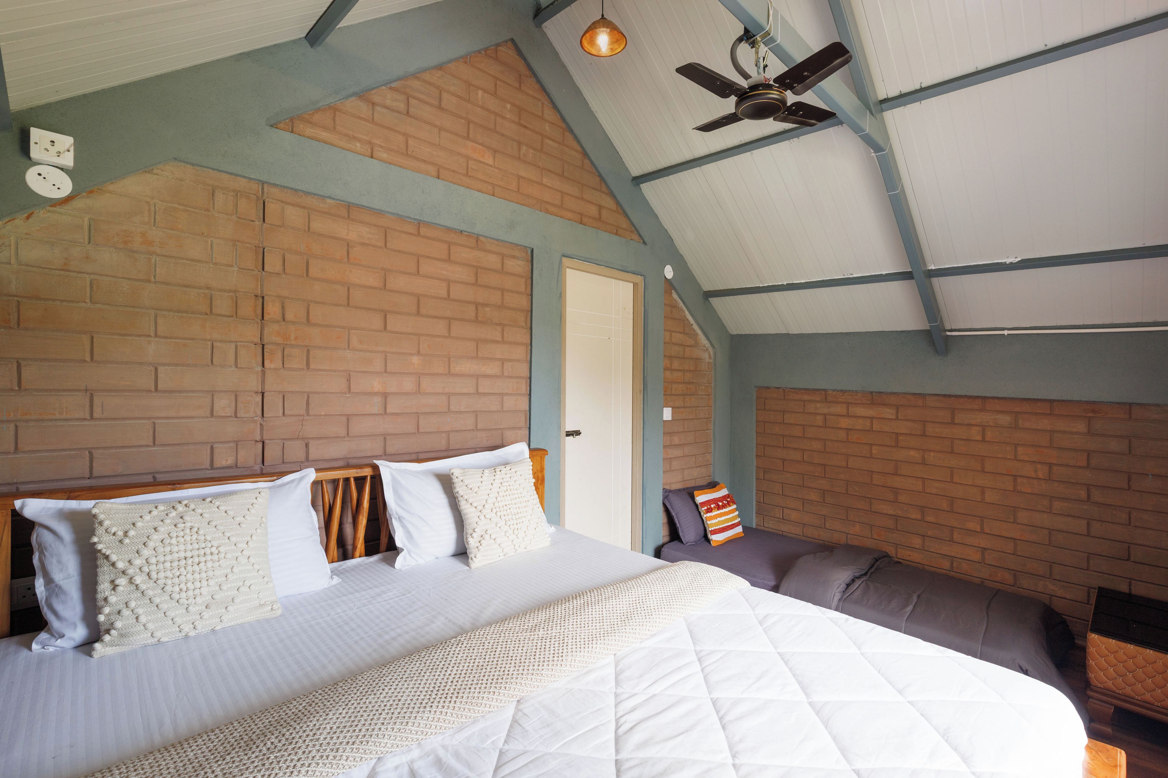 A bedroom with a brick wall, a bed with white bedding, a ceiling fan, and a door.