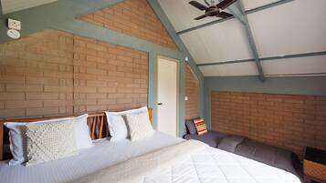 A bedroom with a brick wall, a bed with white bedding, a ceiling fan, and a door.