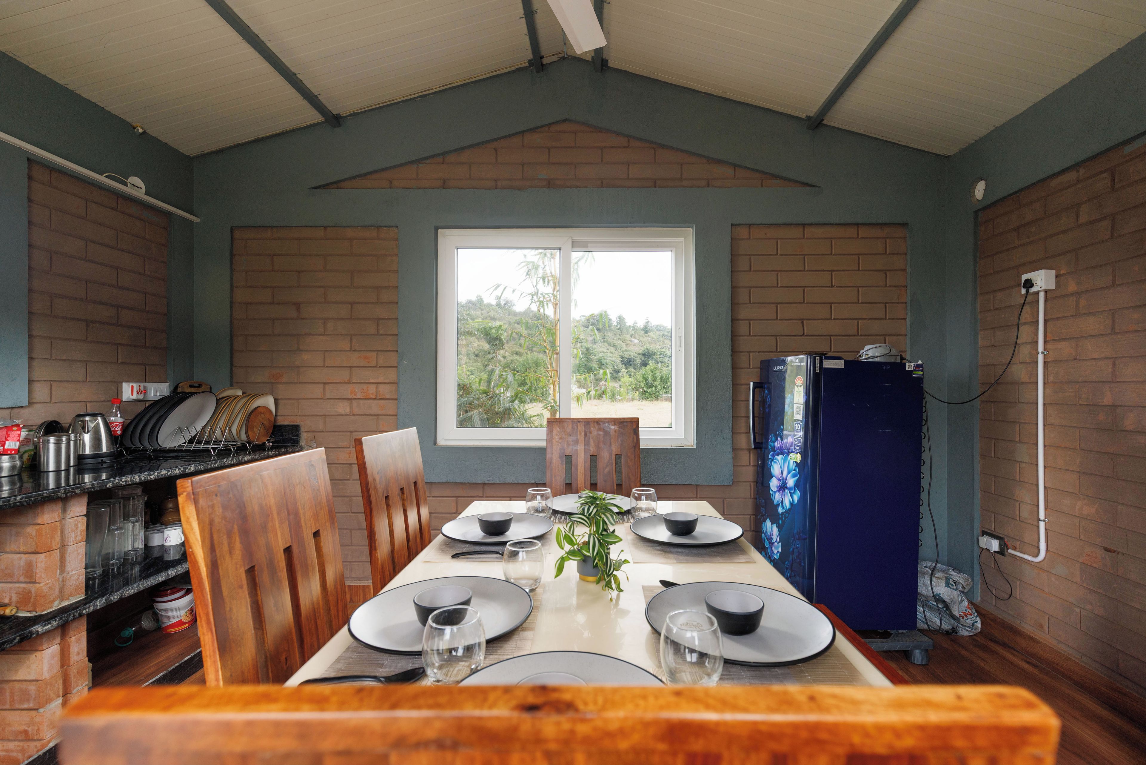A dining area with a table set for four, a brick wall, a window, and a kitchen area with a refrigerator.