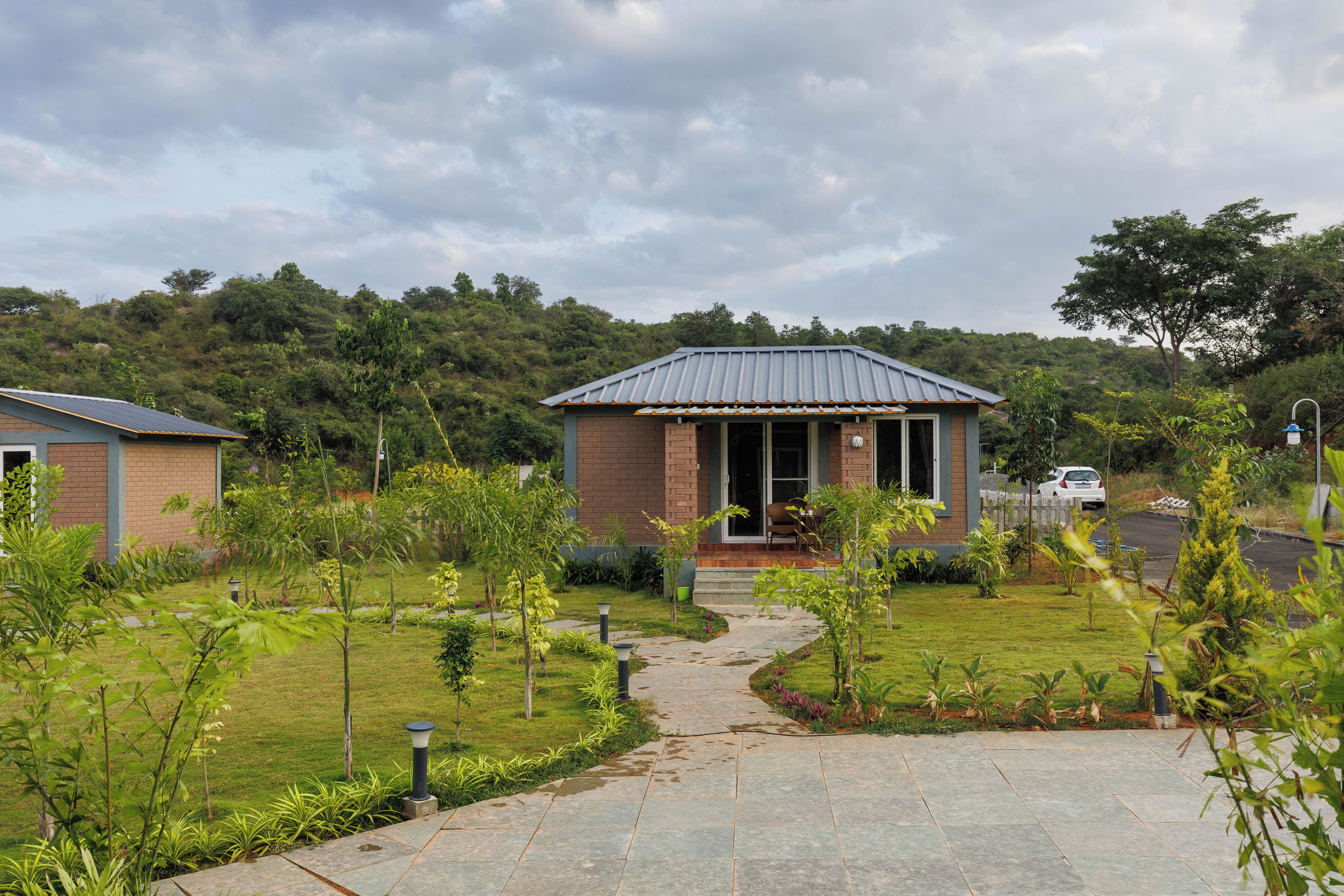A small building with a porch, surrounded by a well-maintained garden and a paved pathway leading to it.