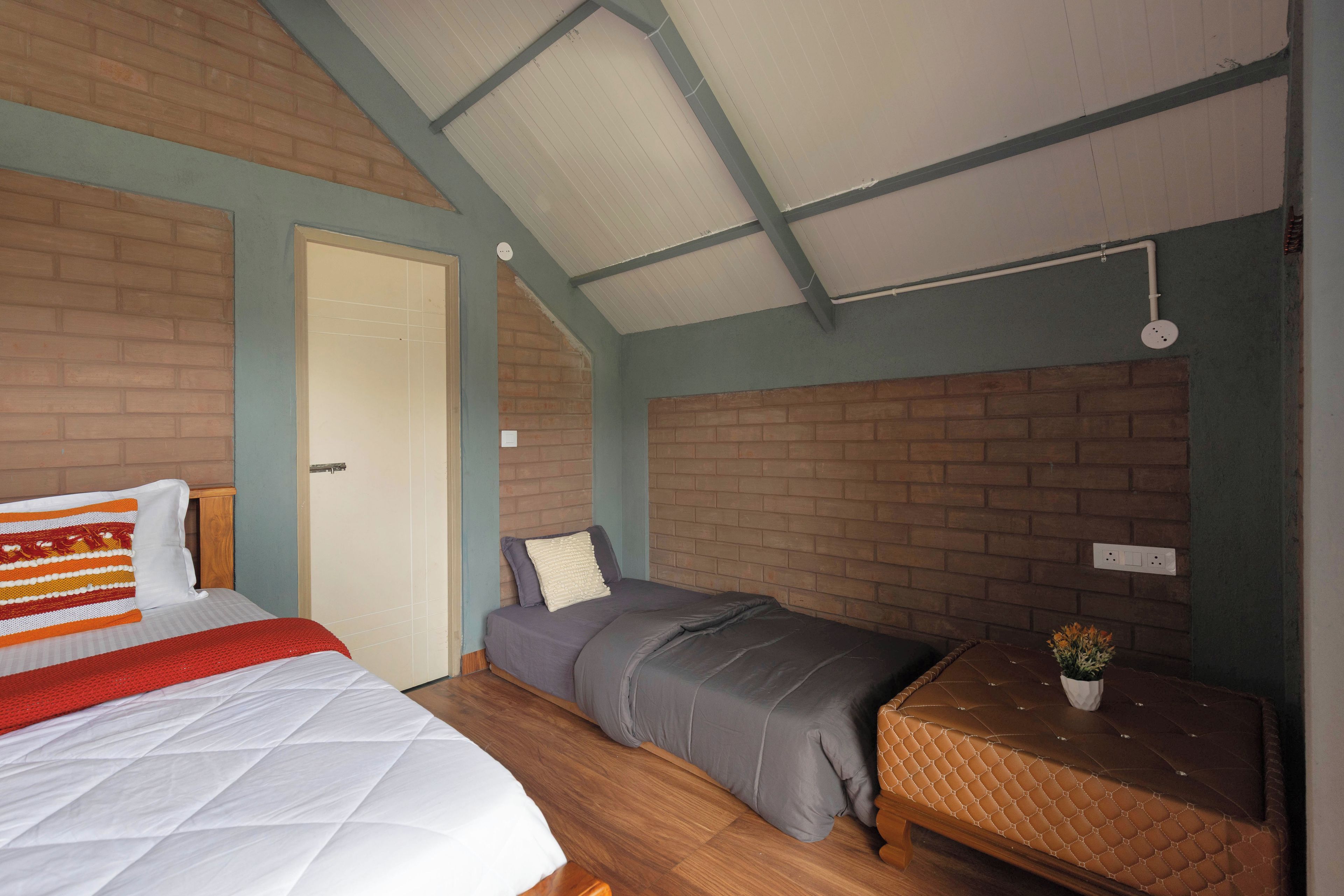 A room with a bed, a smaller bed, a wooden floor, a brick wall, and a ceiling with a skylight.