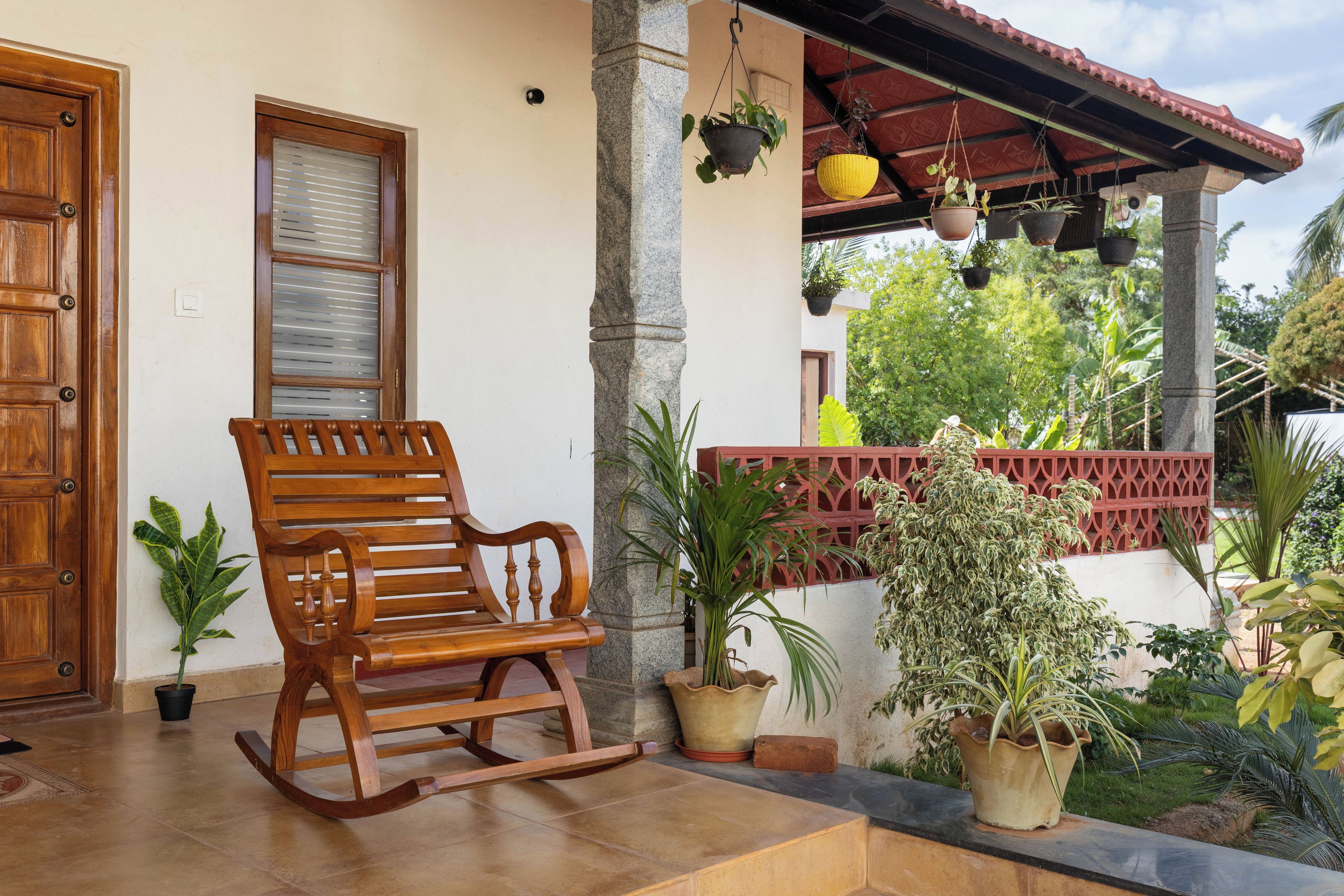 A wooden rocking chair on a tiled porch with potted plants and a red railing.