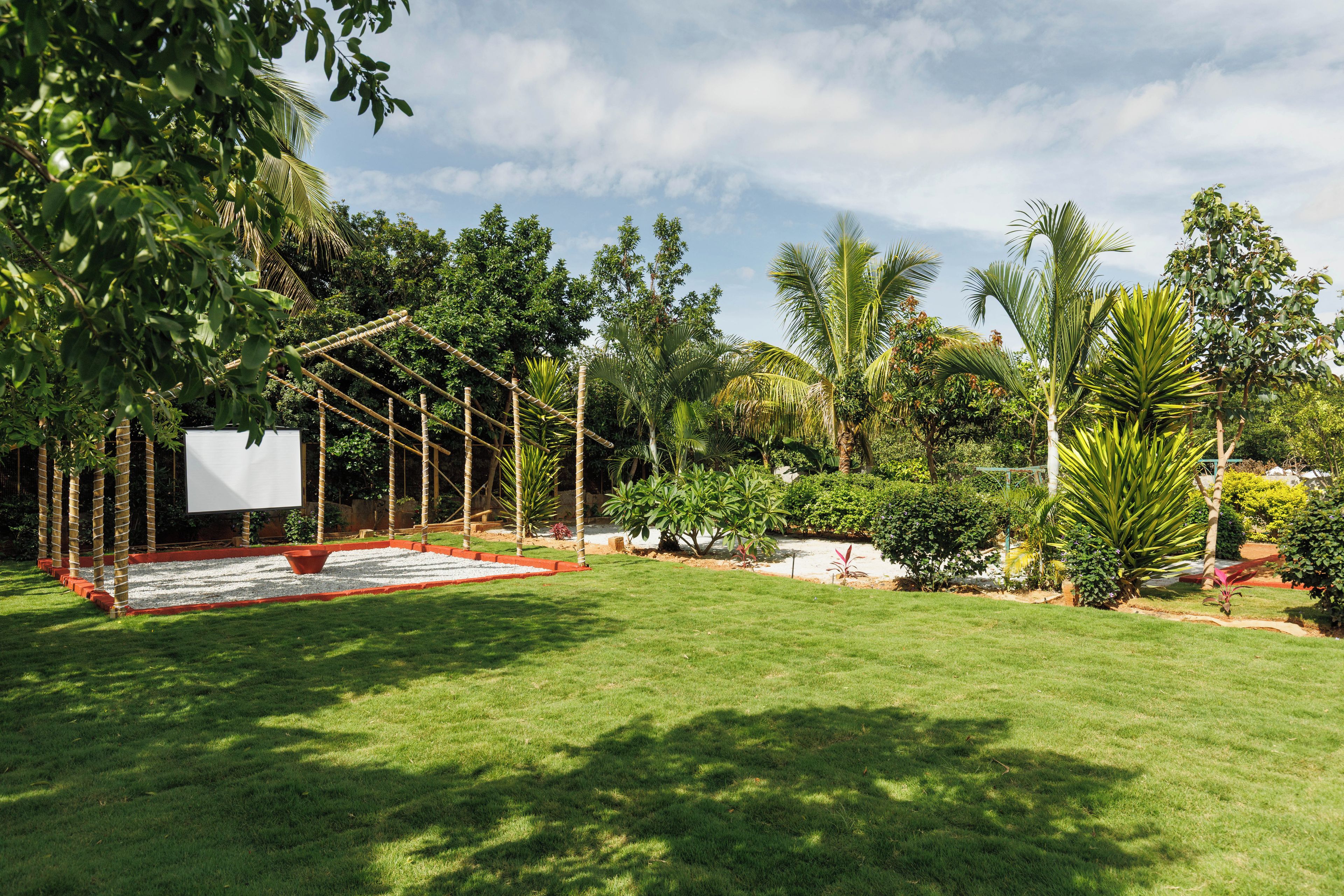 Un jardín bien cuidado con un columpio, un pequeño estanque y diversas plantas tropicales.