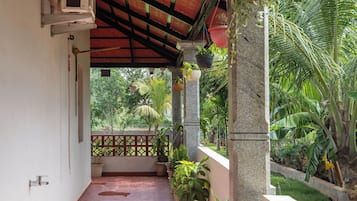 A covered corridor with potted plants, a tiled floor, and a view of greenery outside.