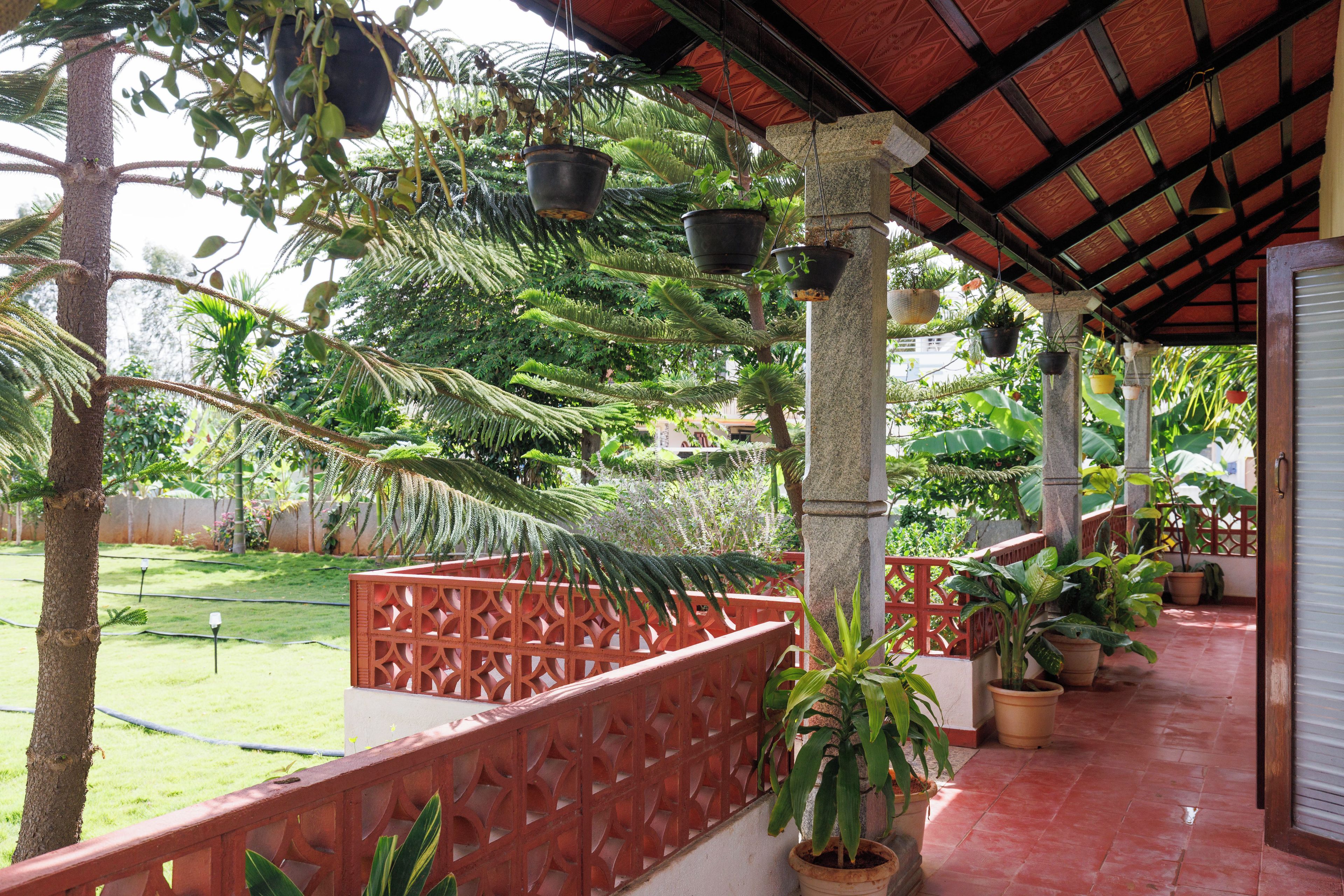 A covered outdoor area with potted plants, a red fence, and a tiled floor.