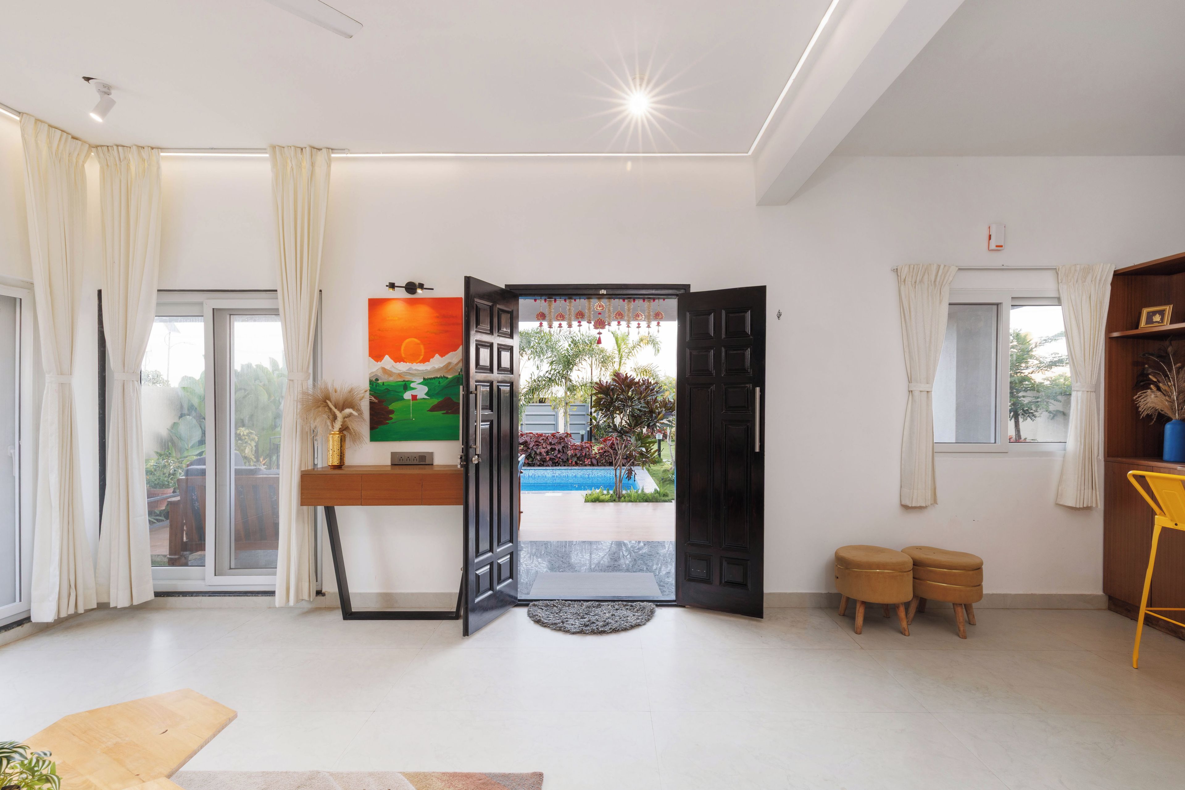 A modern living room with a large window, a painting, a door leading outside, and a small outdoor area visible through the door.