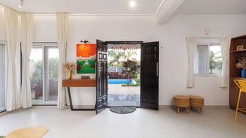 A modern living room with a large window, a painting, a door leading outside, and a small outdoor area visible through the door.