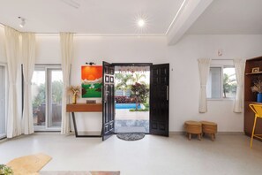 Una sala de estar moderna con un ventanal grande, un cuadro, una puerta que da al exterior y un pequeño espacio al aire libre visible a través de la puerta.