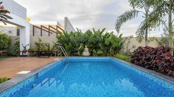 A swimming pool with a tiled edge, surrounded by plants and a building structure.