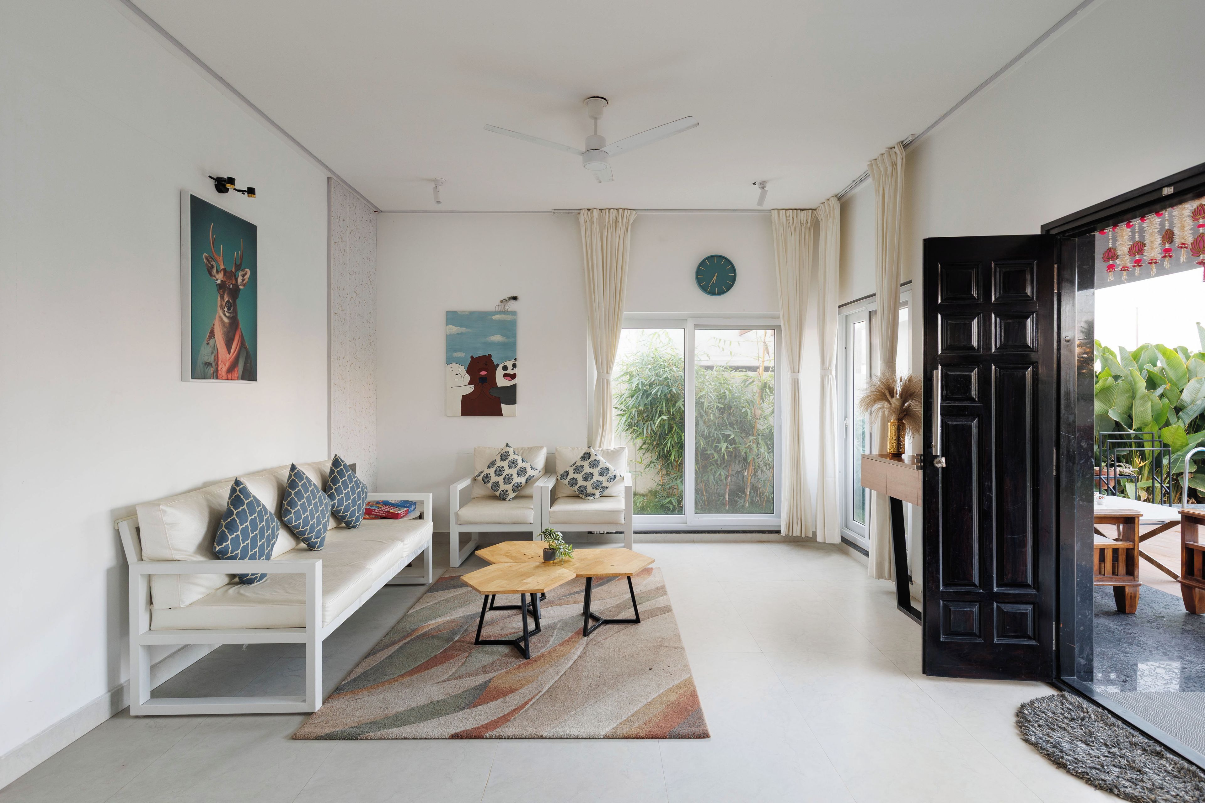 A modern living room with a white sofa, a coffee table, and a large window with a view of greenery.