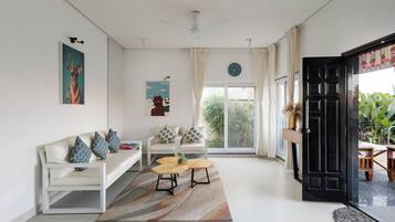 A modern living room with a white sofa, a coffee table, and a large window with a view of greenery.