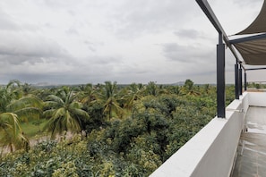 A balcony with a view of a lush landscape, including palm trees and other vegetation. - Sierramystique by Stayjadepool3bhk35min Airport (Doddaballapur)