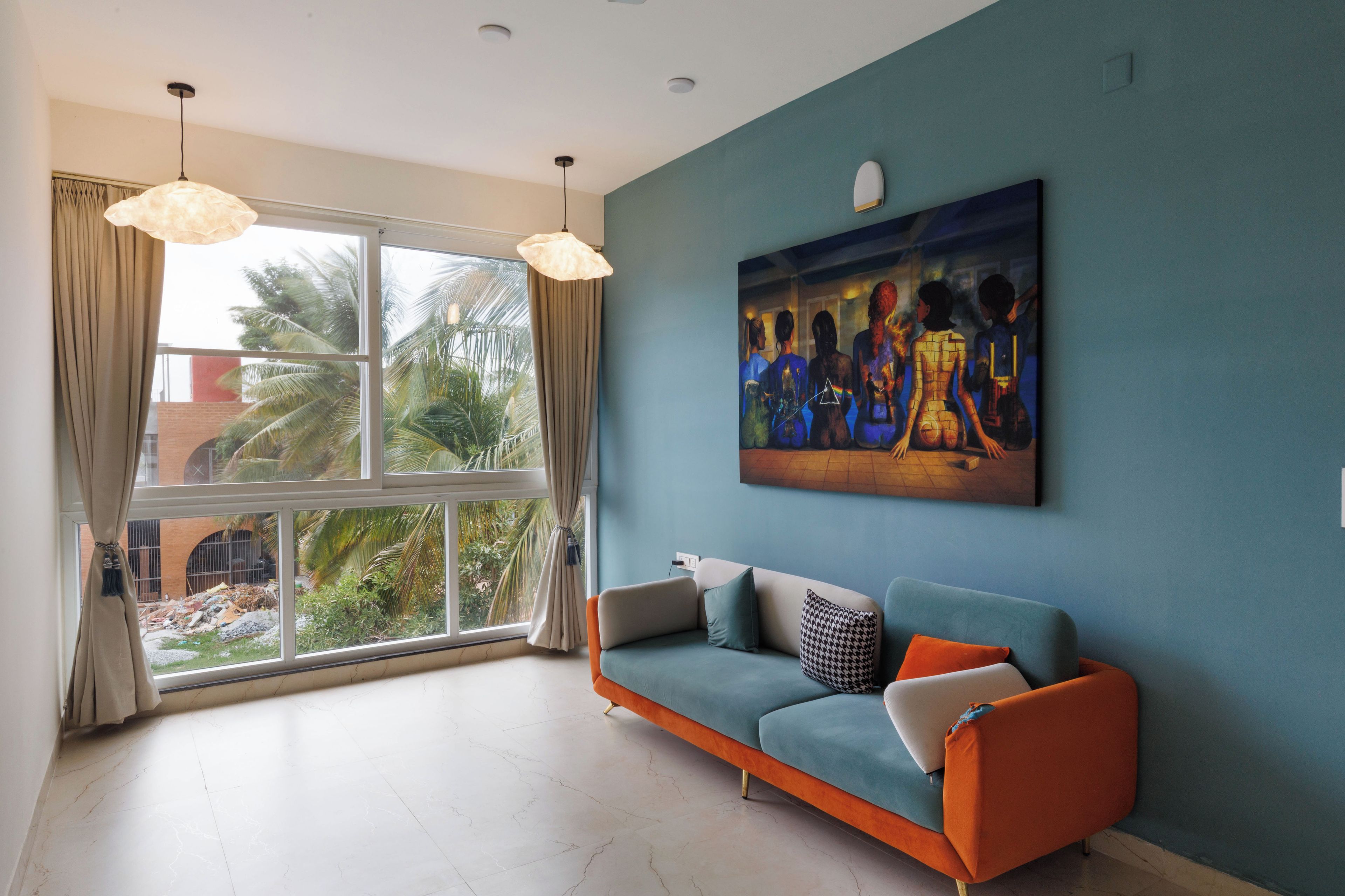 Una sala moderna con un ventanal grande, una pared azul y un sofá con cojines naranja.