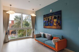 Una sala moderna con un ventanal grande, una pared azul y un sofá con cojines naranja.