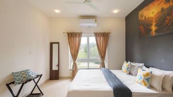 A bedroom with a bed, a chair, a ceiling fan, and a painting on the wall.