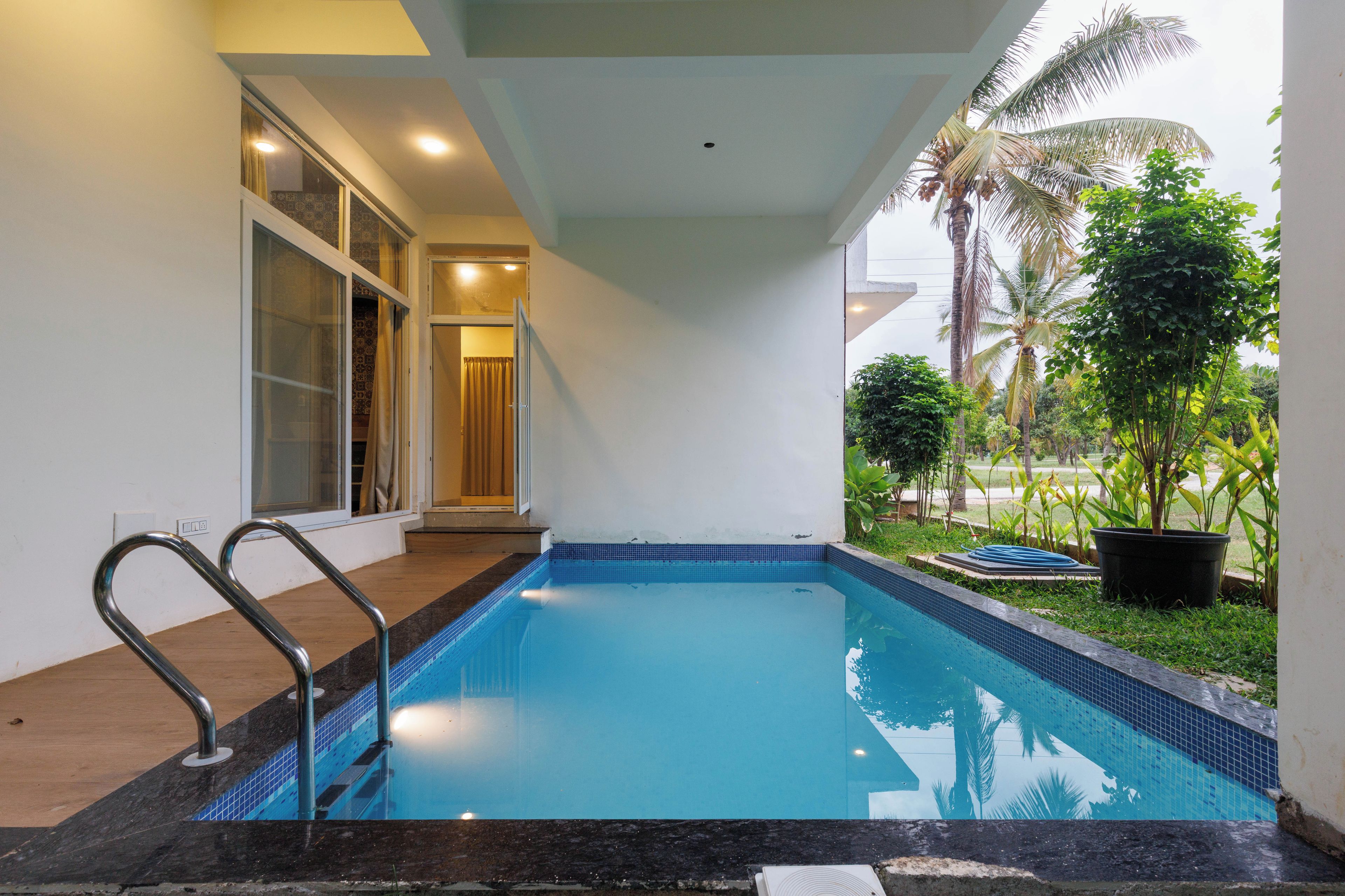 A swimming pool with a tiled edge, a metal ladder, and a glass door leading to a covered area.