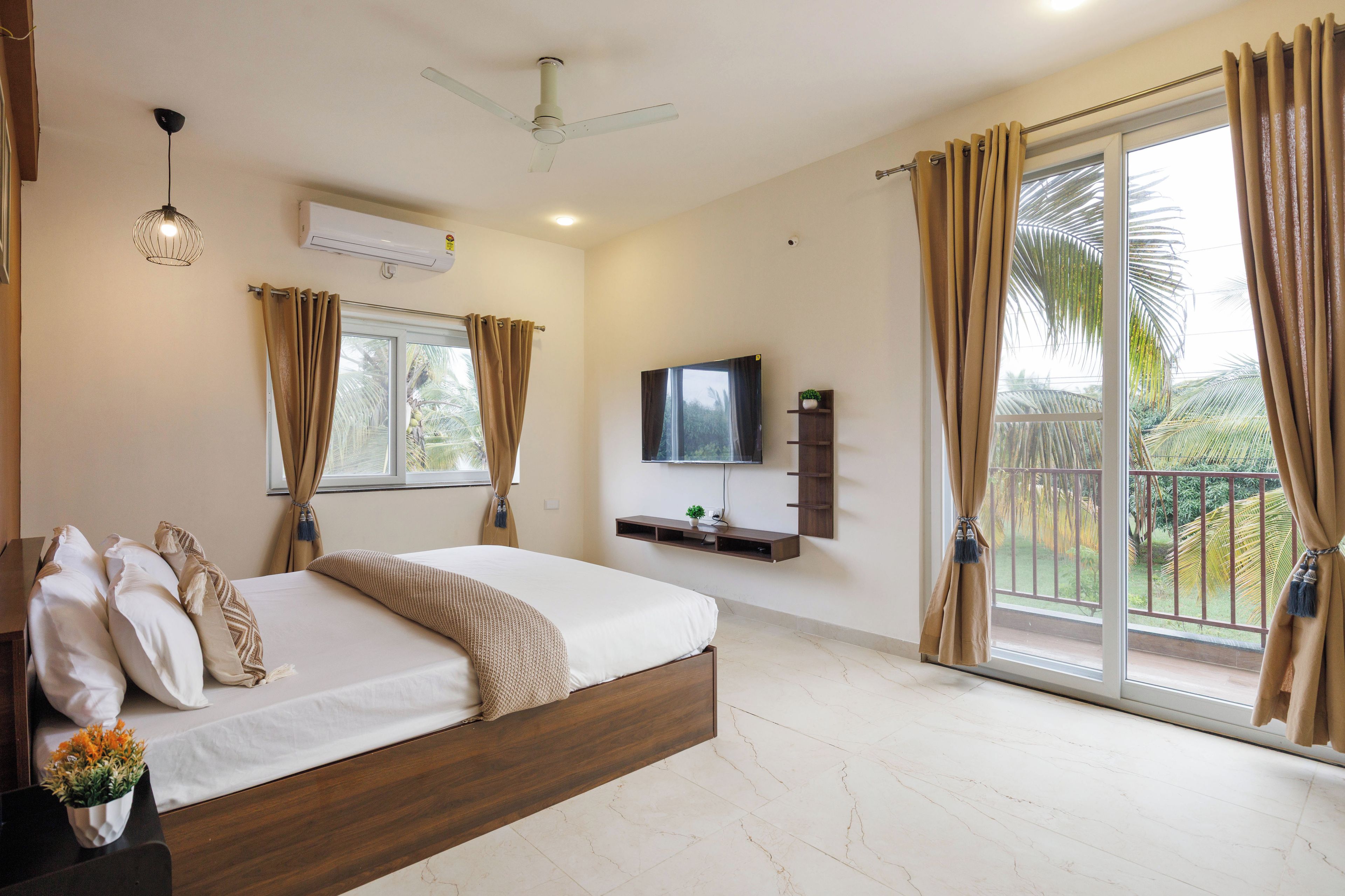 A bedroom with a bed, a ceiling fan, a mounted TV, and a balcony with curtains.