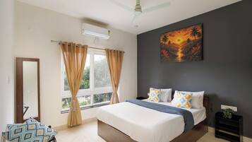A bedroom with a bed, curtains, a ceiling fan, a painting, and a window with a view of greenery.