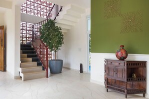 A staircase with a metal railing, a potted plant, and a wooden cabinet with a decorative vase. - Sierramystique by Stayjadepool3bhk35min Airport (Doddaballapur)