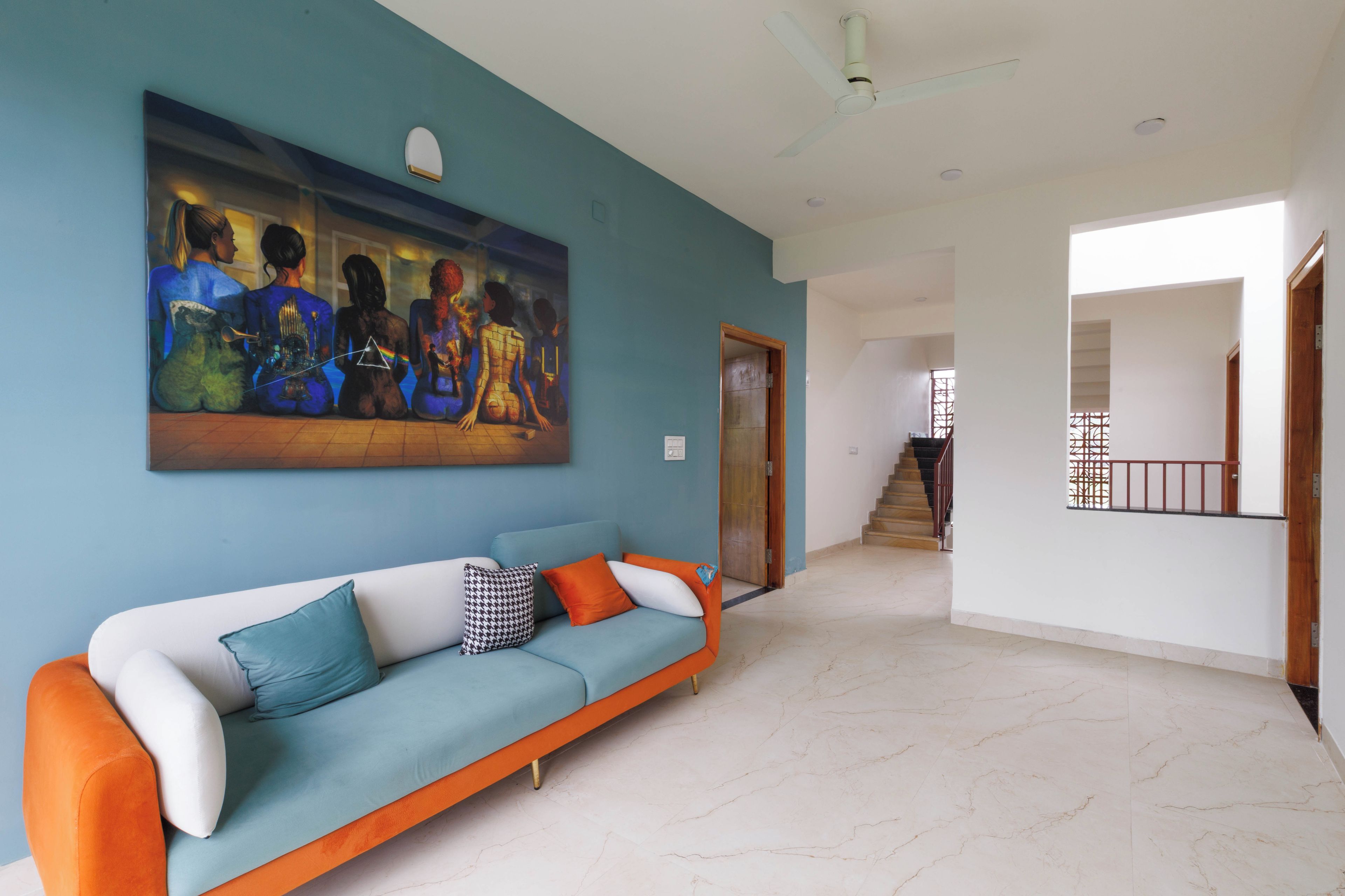 A living room with a sofa, a painting, and a staircase leading to another room.