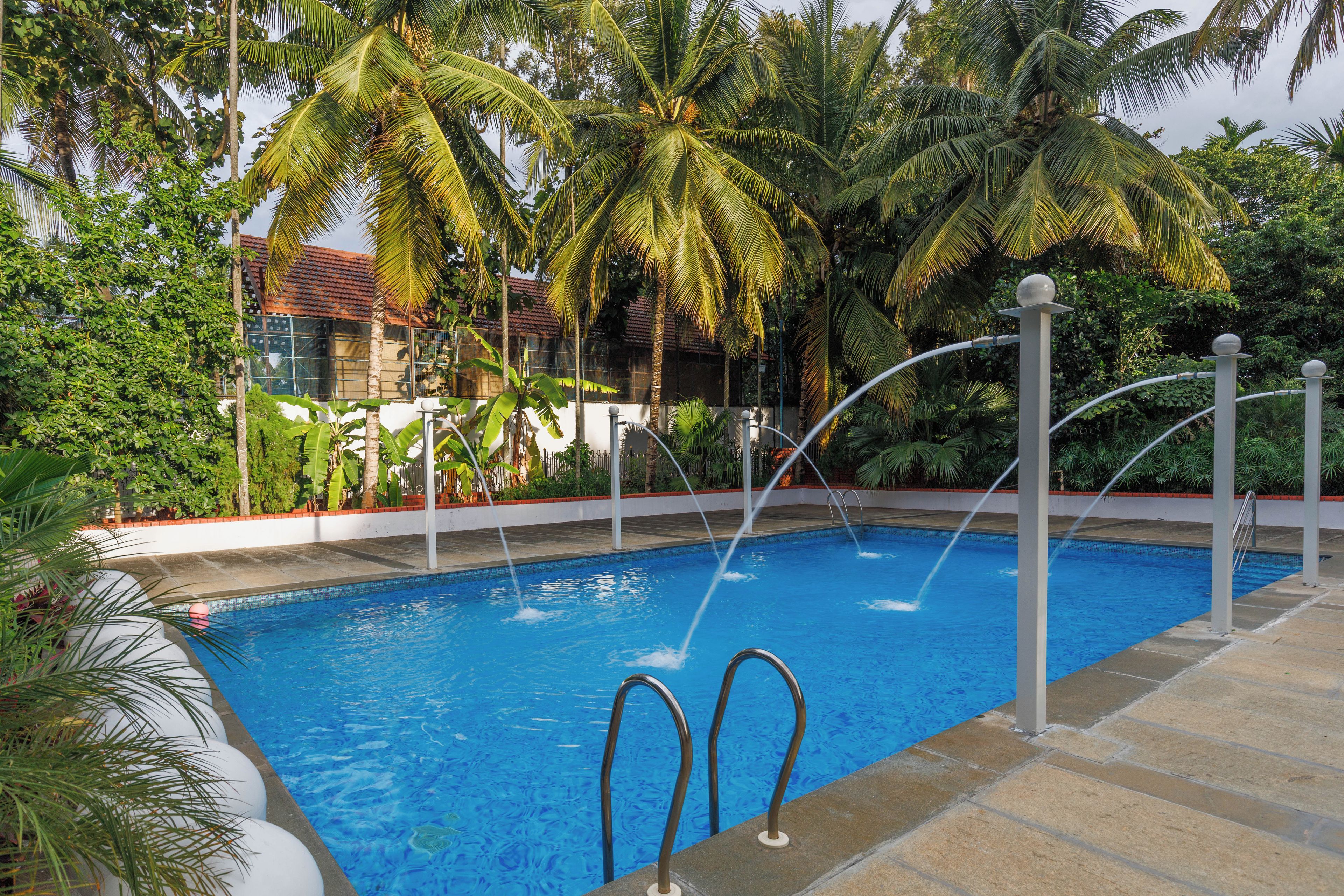 Una piscina con dos escaleras, rodeada de palmeras y un edificio con tejado de azulejos.