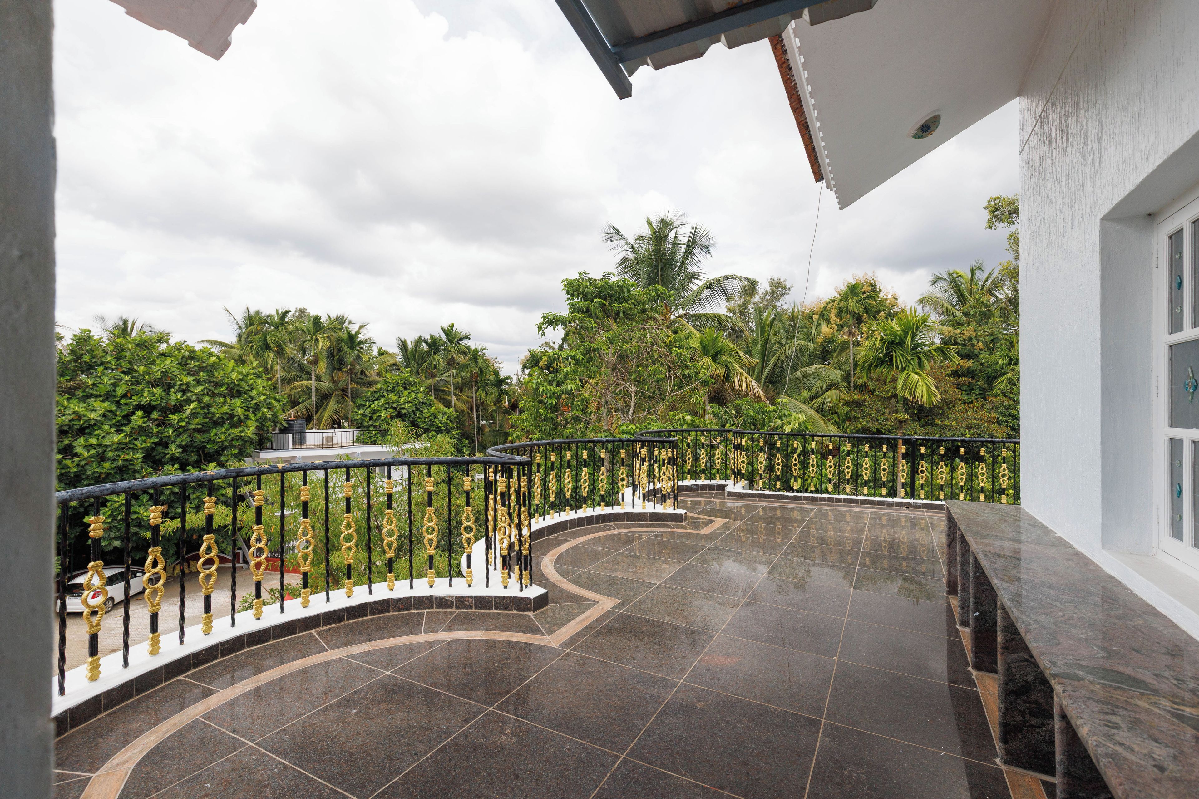 A curved balcony with a reflective tiled floor, surrounded by lush greenery and a white building.