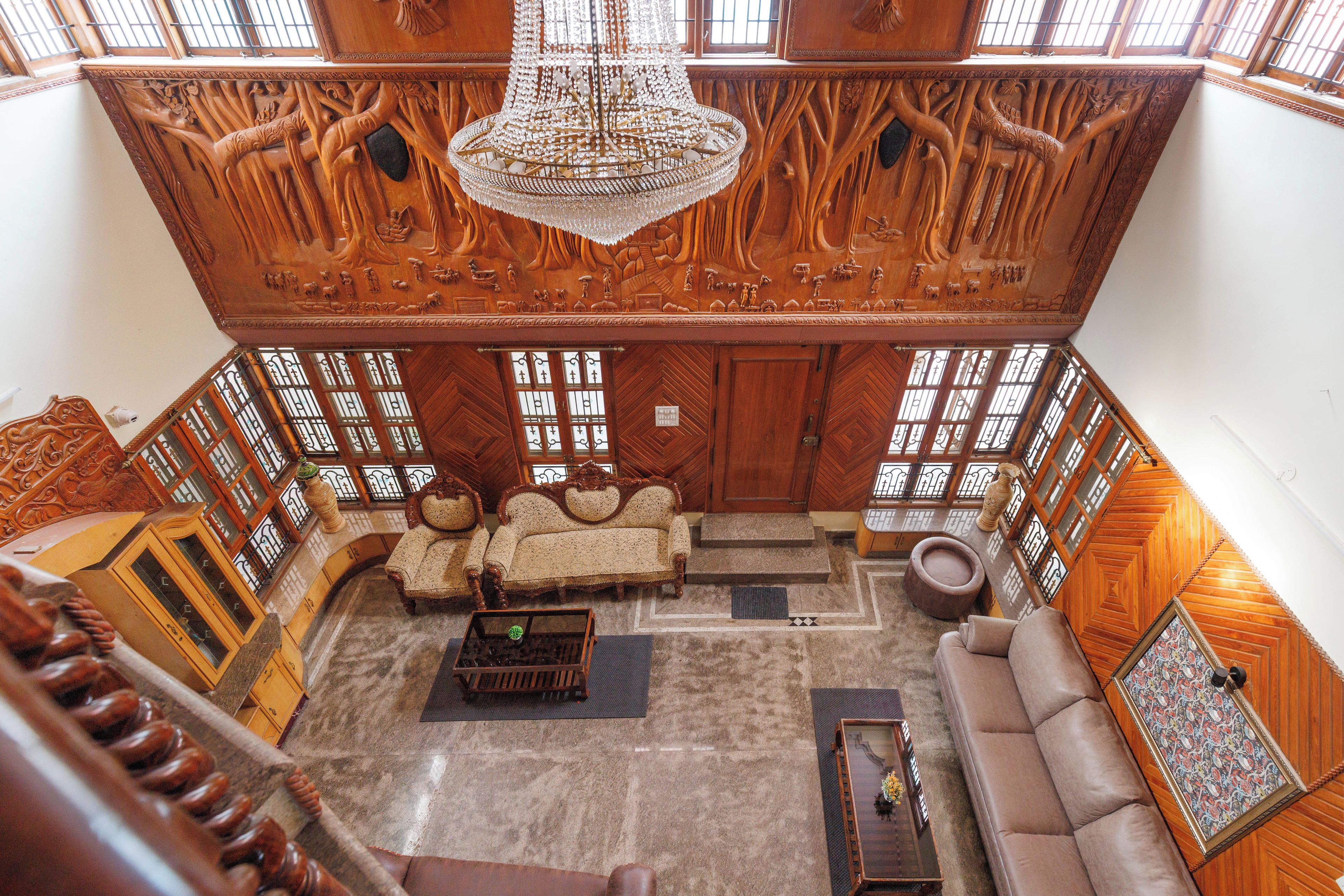 Una habitación amplia con techo alto, elaboradas esculturas de madera, un candelabro y un ventanal grande.