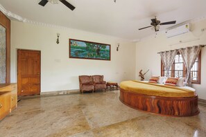 Un dormitorio amplio con una cama grande, ventilador de techo, equipo de aire acondicionado, un cuadro en la pared y una ventana con cortinas.