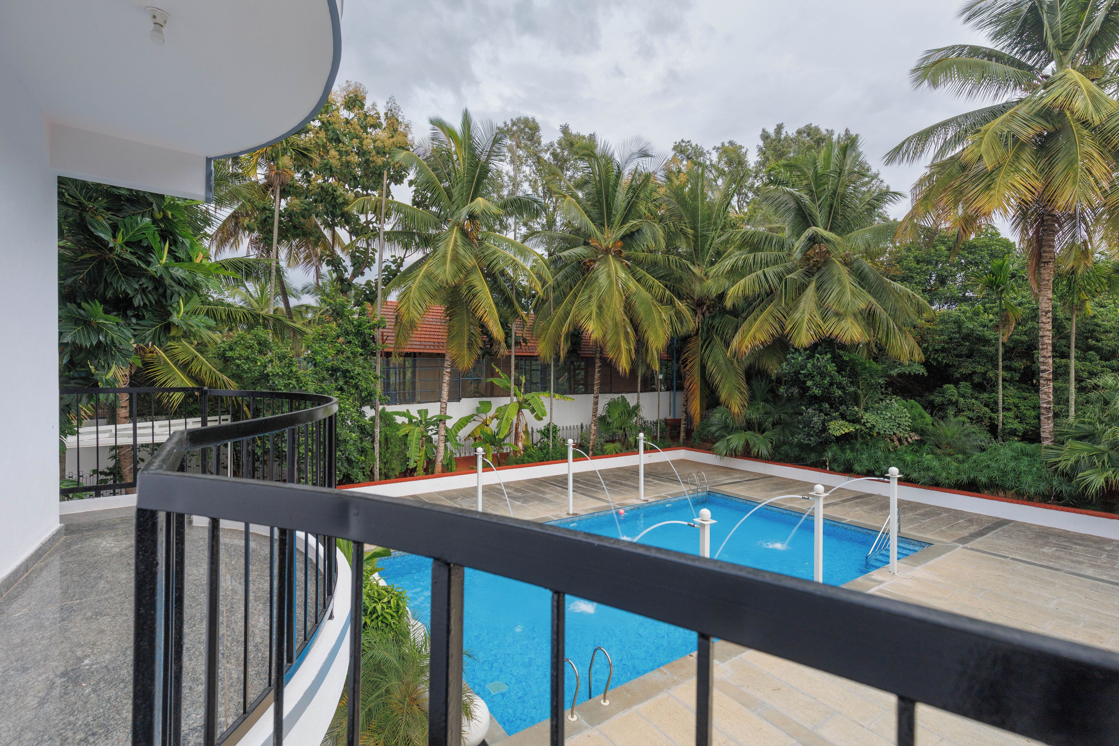 A pool area with a clear blue pool, surrounded by palm trees and a white building with a red roof.