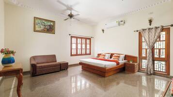 A bedroom with a bed, a sofa, a ceiling fan, a window with a curtain, and a painting on the wall.