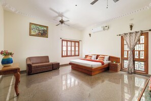 Un dormitorio con cama, sofá, ventilador de techo, ventana con cortina y un cuadro en la pared.