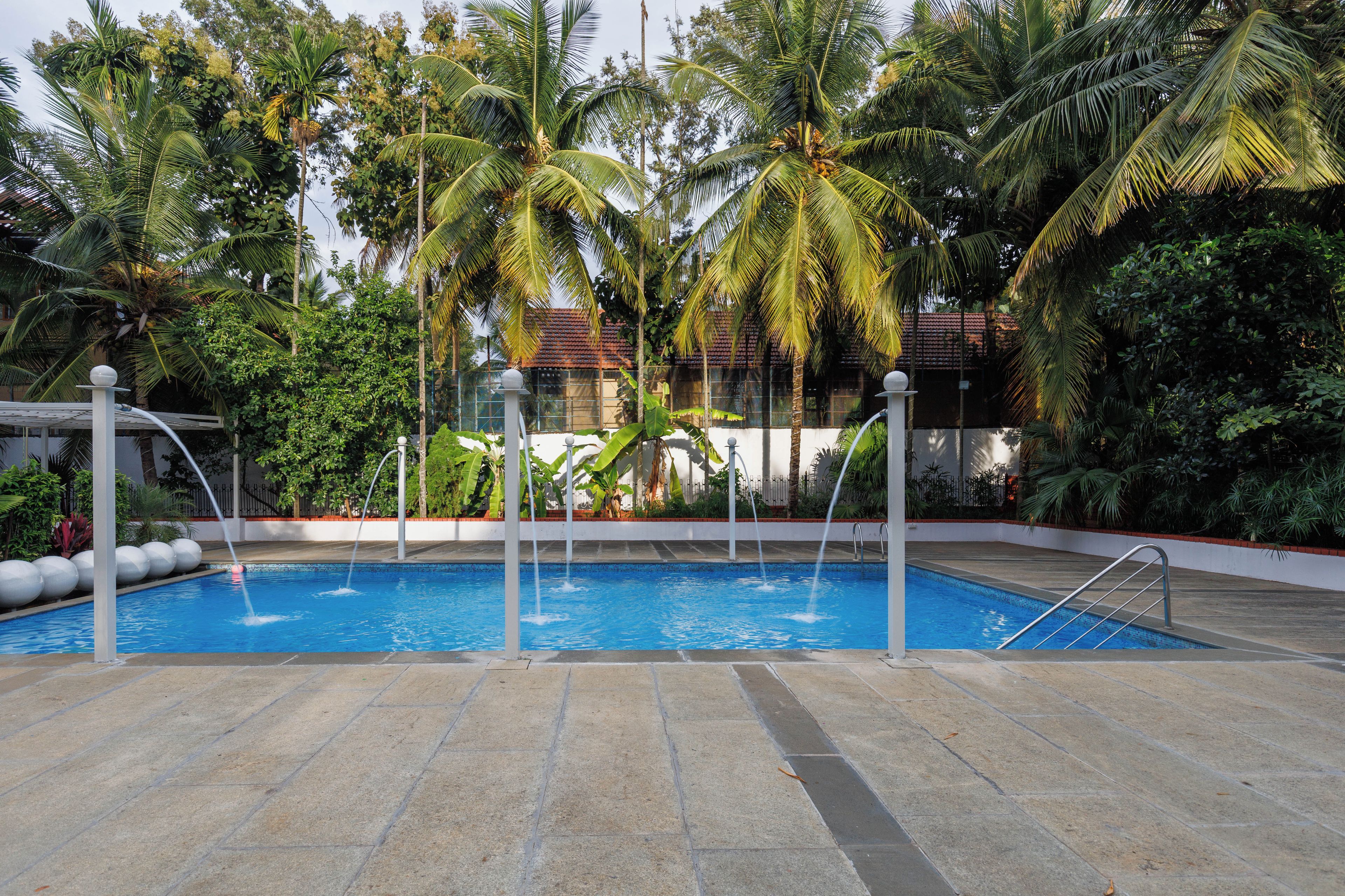 Une piscine dotée d’une terrasse carrelée, entourée de palmiers et bordée d’un bâtiment dont le toit est recouvert de tuiles rouges.