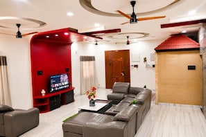 A modern living room with a sectional sofa, a flat-screen TV, and a ceiling fan. - Nectar by Red Olive 3bhk ECR IT Park OMR (Chennai)