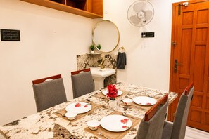 A dining area with a marble table, chairs, a mirror, a fan, and a wooden door. - Nectar by Red Olive 3bhk ECR IT Park OMR (Chennai)