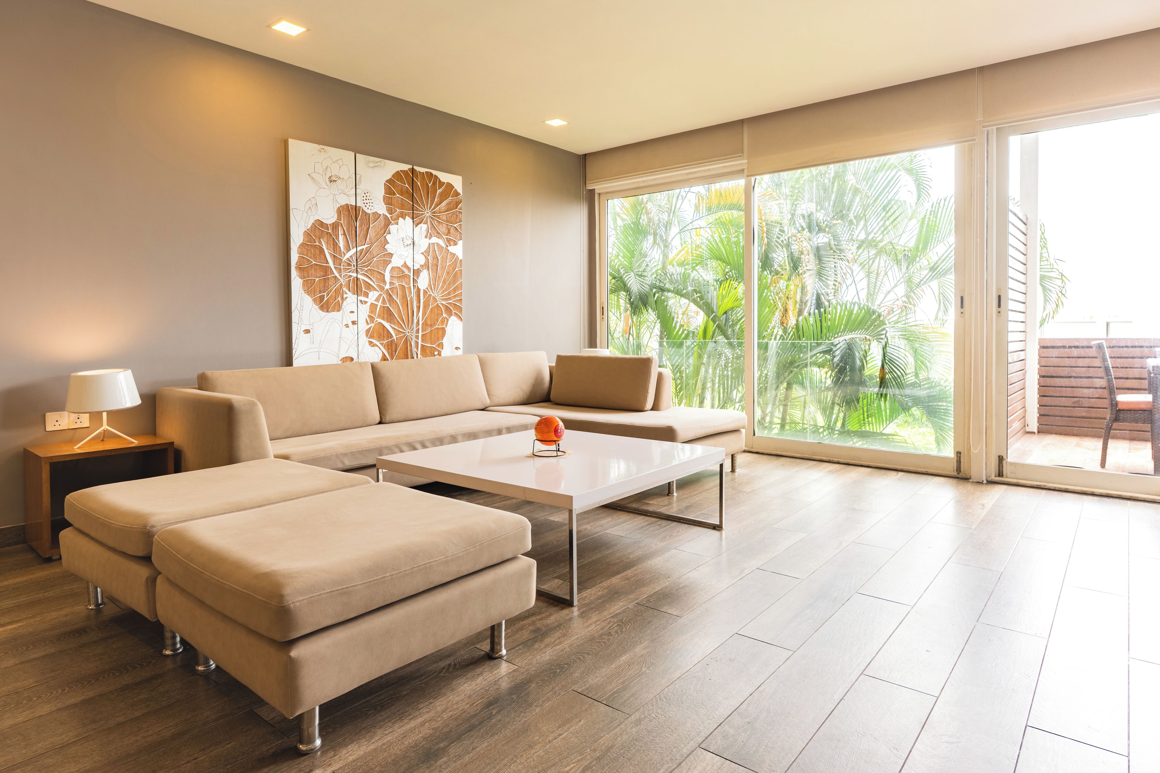 A modern living room with a sectional sofa, a coffee table, and a large window with a view of palm trees.