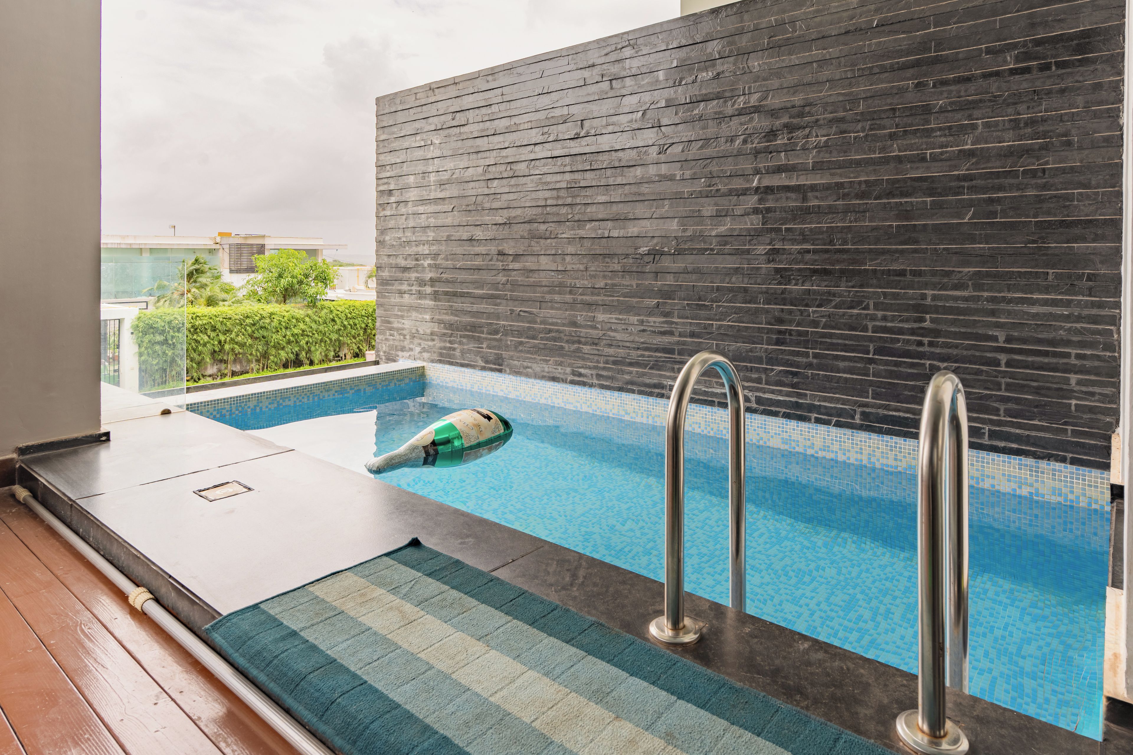 A swimming pool with a tiled floor, metal handrails, and a view of a building in the background.