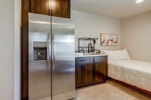 Ein kompaktes Hotelzimmer mit einem fest eingebauten Kühlschrank, einer kleinen Küchenzeile inklusive Spüle und einem Bett mit weißer Bettdecke.