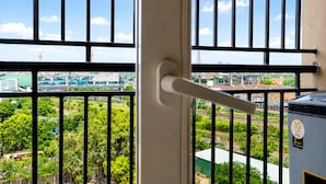 Une vue à travers une fenêtre ornée d’une rambarde en métal, avec une poignée de porte et un réservoir d’eau portant une étiquette.