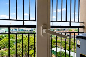 A view through a window with a metal railing, a door handle, and a water tank with a label. - The Icon by Redolive 2bhkkoyambeduit Parkdlf (Chennai)