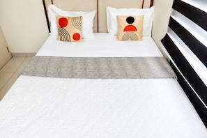 A neatly made bed with a patterned bedspread and two pillows with abstract designs.