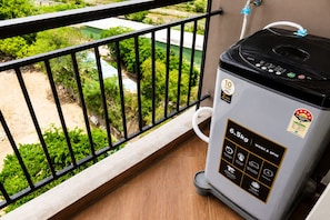 A portable washing machine on a balcony with a view of greenery and a paved area.