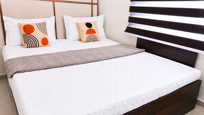 Un lit avec un matelas matelassé blanc, deux oreillers à motifs géométriques et un plaid marron.