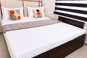 A bed with a white quilted mattress, two pillows with geometric patterns, and a brown throw blanket. - The Icon by Redolive 2bhkkoyambeduit Parkdlf (Chennai)