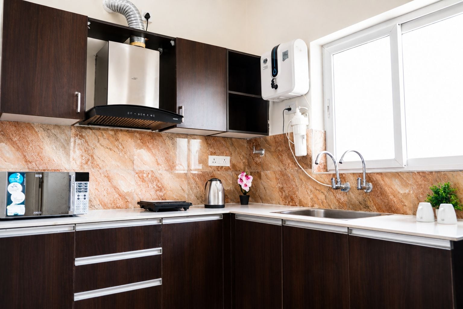Une cuisine moderne avec des meubles de couleur bois foncé, une hotte de cuisinière en acier inoxydable, un four à micro-ondes et un distributeur d’eau intégré.