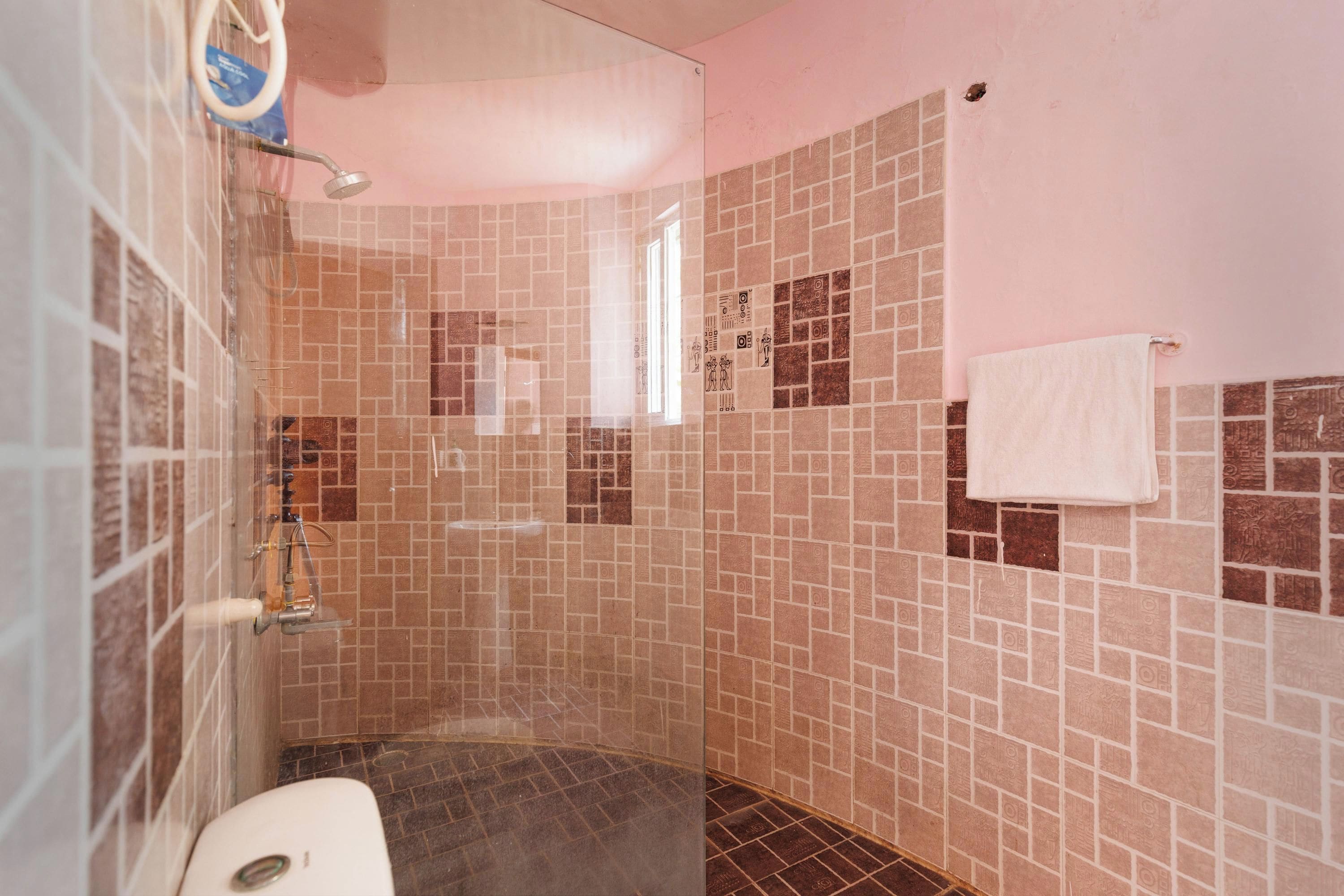 A shower with a glass door, tiled walls, and a white towel hanging on the wall.