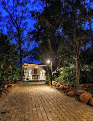 A paved pathway leading to a building with a pool, surrounded by trees and rocks.
