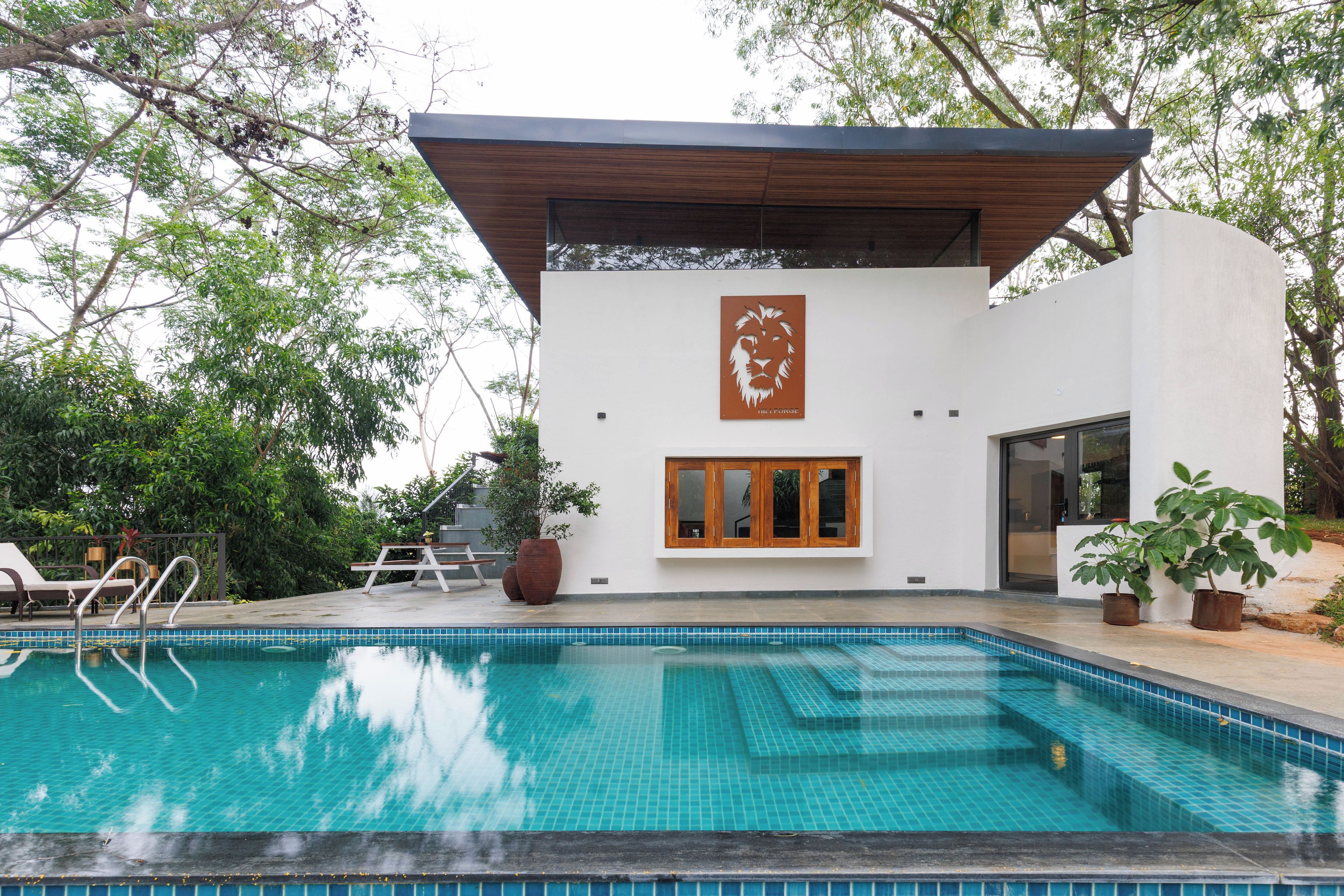 Un área moderna junto a la piscina con una piscina cristalina, una terraza de madera y un edificio blanco con un mural de león.